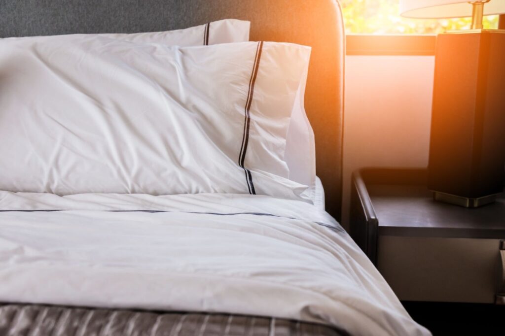 Perfectly made bed with triple-folded sheets and fluffed pillows in morning light