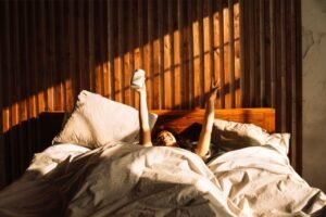 Alt Text: A person enjoying a peaceful morning stretch in a sunlit bed made with pristine white cotton sheets, illustrating the comfort of well-cared-for bedding.