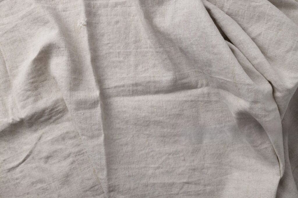 A close-up, textured shot of an old, well-loved linen sheet. You can see the subtle slub of the fabric, the soft wrinkles, and the gentle fading of the color, telling a story of years of use and care.]