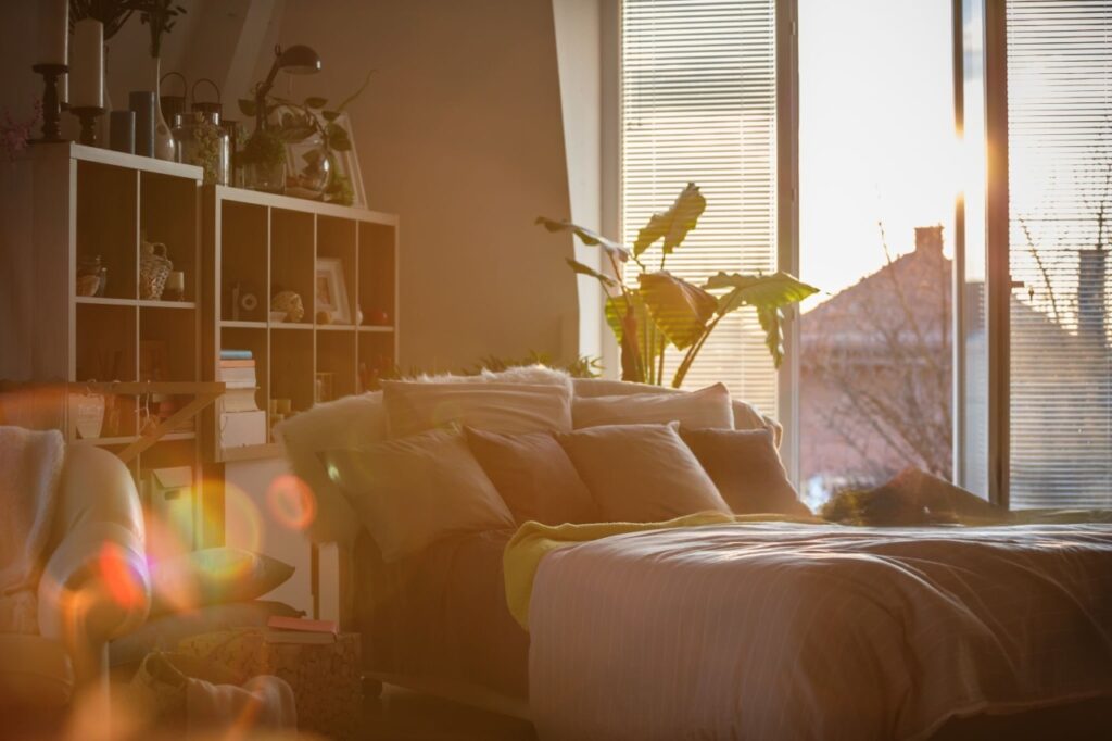 A serene, sun-drenched bedroom in the morning light. The bed is beautifully made with Humā linen, the fabric rumpled and soft. A cup of steam coffee sits on a nightstand, and the scene evokes a feeling of peace and quiet rejuvenation